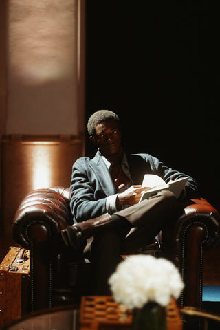 Intimate portrait of a guest in the evening lounge of a five-star hotel: a man sits relaxed on a brown Chesterfield armchair, reading a book, wearing a blazer over a checked shirt and brown trousers