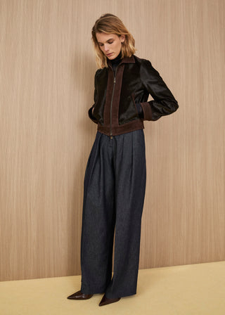 Short zippered bomber jacket in glossy dark brown calf hair with suede trim, dark indigo wide-leg denim trousers with deep front pleats, and dark brown pointed shoes