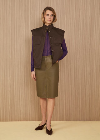 Model wearing a structured dark brown high-neck vest, a sheer electric purple knit top, an olive green leather midi skirt with a front slit, and dark pointed heeled slingbacks