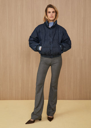 Model wearing a padded puffer jacket in dark blue denim, a light blue turtleneck sweater, flared trousers in a grey and beige micro-check pattern, and dark brown pointed heels