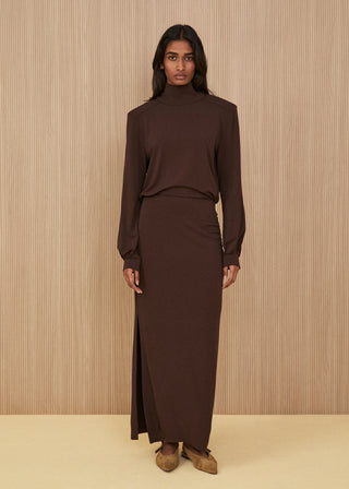 Chocolate brown co-ord set featuring a fluid high-neck top and a matching long maxi skirt with a deep side slit, paired with light taupe pointed suede shoes