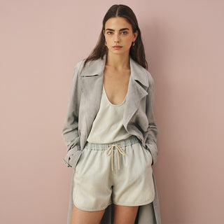 Model wearing a light blue suede trench coat over a matching scoop-neck top and drawstring shorts in a tonal washed finish
