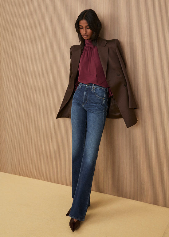 Model wearing a brown double-breasted blazer, burgundy high-neck blouse, straight jeans, and brown leather heeled shoes