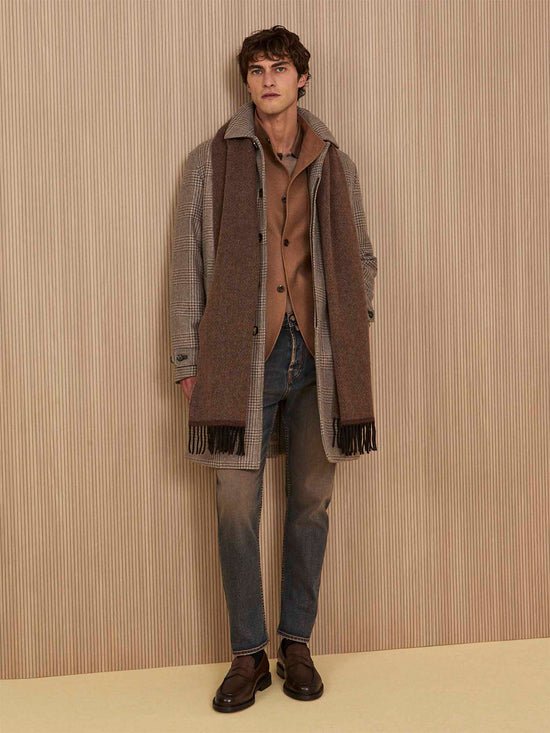 Model wearing a grey houndstooth coat, brown fringed scarf, camel blazer, jeans, and brown leather loafers