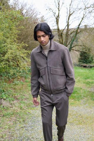 Man walking outdoors in a taupe-brown zip-up jacket with chest pockets, a beige turtleneck and matching tailored trousers