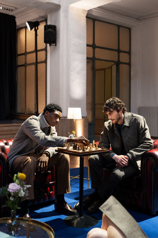 Intimate scene in the lobby of a five star hotel: two guests are playing chess, seated in leather Chesterfield armchairs, with a chessboard set on a gilded side table