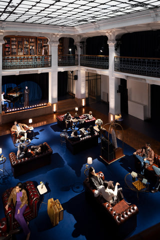 Evening scene in the lobby of a five-star hotel: a spacious hall with blue carpeting, brown leather Chesterfield sofas, and burgundy armchairs