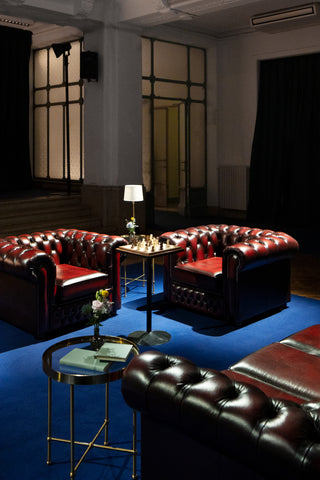 Intimate lounge area of a five star hotel with evening lighting: an arrangement of leather Chesterfield sofas and armchairs on blue carpeting