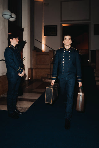 Night time scene in the lobby of a five-star hotel: two models wearing navy blue uniforms with gold piping and braid, and double breasted gold buttons