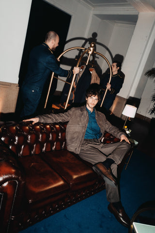 Five-star hotel lobby: a vintage gold luggage cart at the center with two porters in navy-blue and gold uniforms