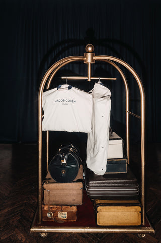 Vintage gold luggage cart in a five-star hotel loaded with antique suitcases and clothing: brass tubular frame with base wheels and a decorative arched top with a sphere