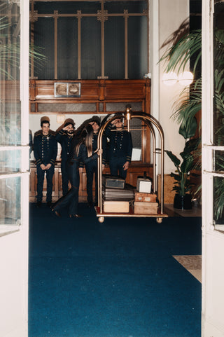 Daytime main entrance of a five star hotel: four staff members in navy-blue uniforms with gold accents stand in front of the reception desk