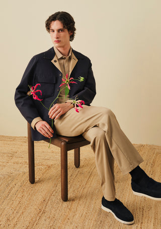 A young man with curly dark hair sits on a wooden stool against a beige background