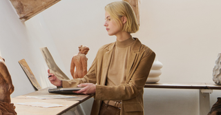 Woman in tonal beige and brown outfit with tailored blazer and wide-leg trousers browsing art exhibition