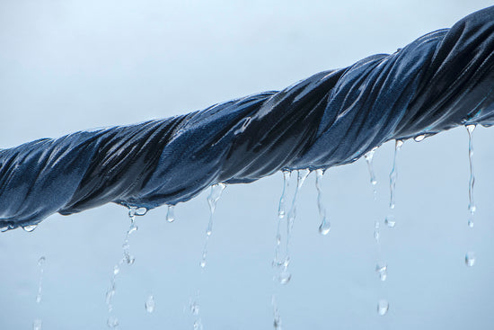 Close-up of a twisted wet rope wrapped in dark blue fabric with water droplets dripping down against a light blue background