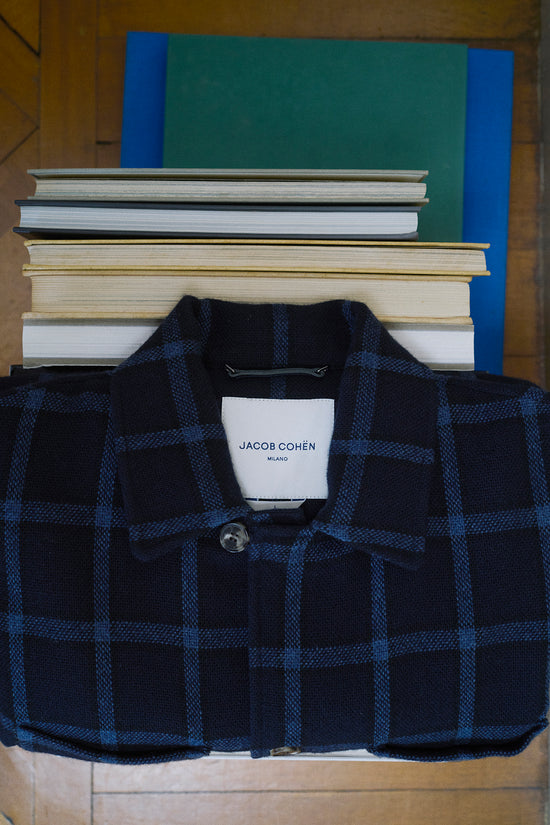 Folded navy checked Jacob Cohën shirt placed on a stack of books, with the brand label visible