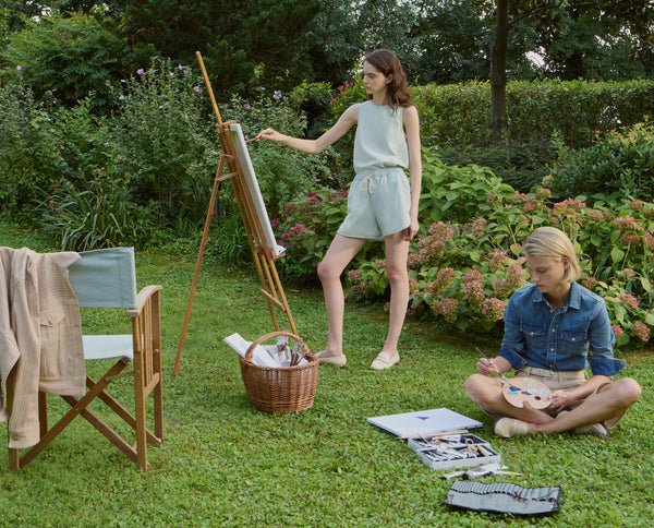 Two women painting outdoors in a lush garden setting