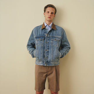 Model wearing a washed blue denim jacket with a contrast collar, paired with taupe linen bermuda shorts and a light blue shirt