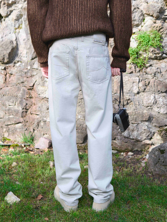 Rear view of high-waisted light-wash jeans paired with brown ribbed knit sweater in outdoor stone wall setting