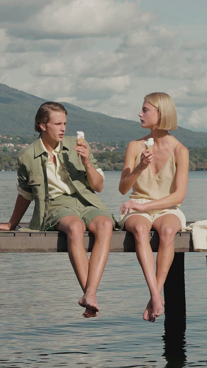 Two young adults wearing casual summer outfits while enjoying ice cream on a lakeside pier.